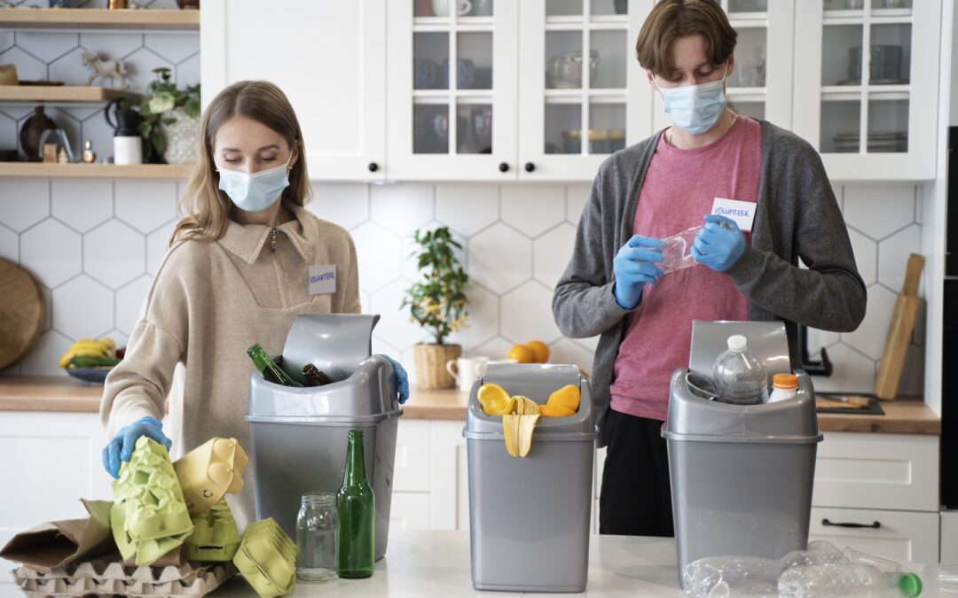 Deux personnes trient des déchets dans une cuisine avec plusieurs poubelles.